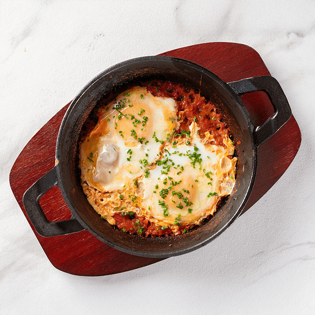 Shakshuka Clásica - Huevos cocidos en salsa de tomates especiada, pimentón y cebolla con pan artesanal en Le Grenier