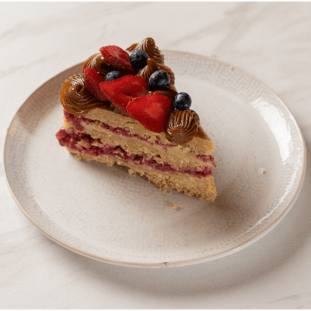 Torta Caluga - Bizcocho suave y húmedo, relleno con una cremosa caluga artesanal de manjar y caramelo, con notas tostadas y un dulzor perfecto, acompañado de pasta de frambuesa que aporta un toque frutal y ácido para un equilibrio delicioso. en Le Grenier